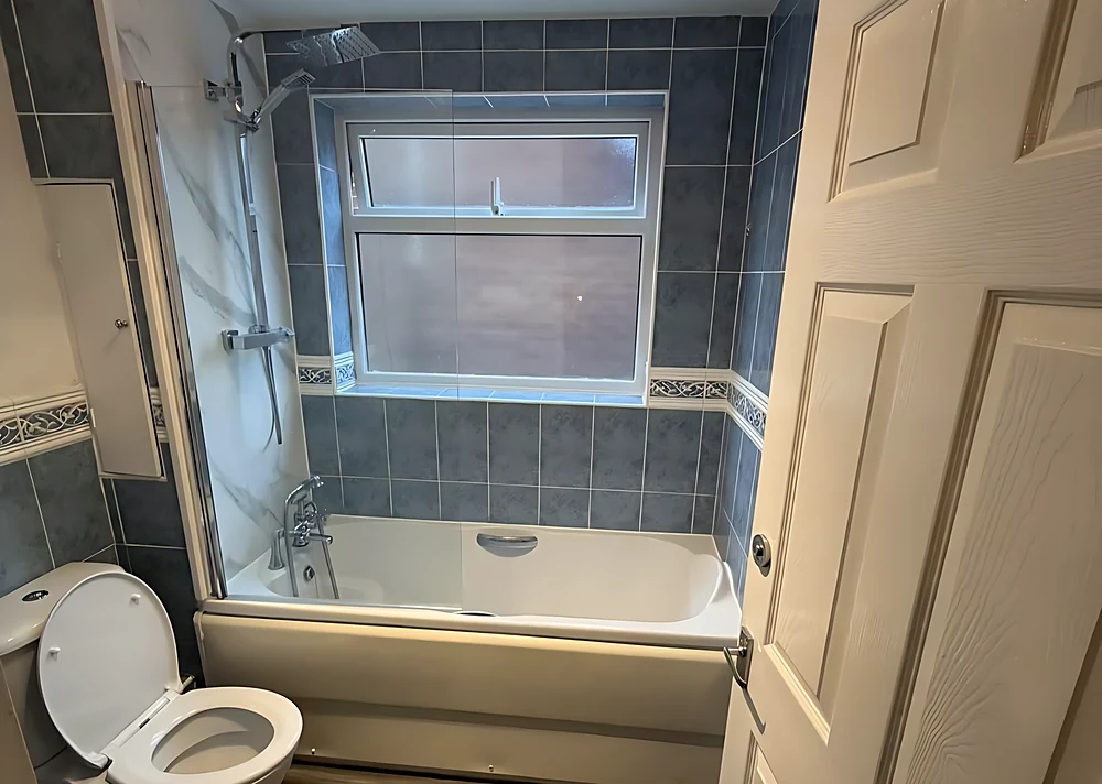 Before: the same Billericay bathroom with a bath, blue tiles and a wood-effect floor