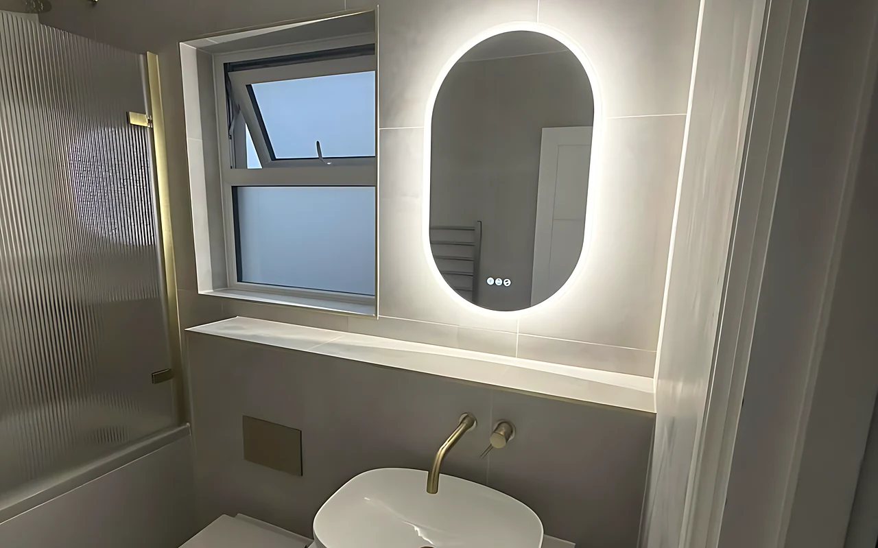 Bathroom with an oval LED mirror, a brushed brass tap and a countertop basin on a wood vanity