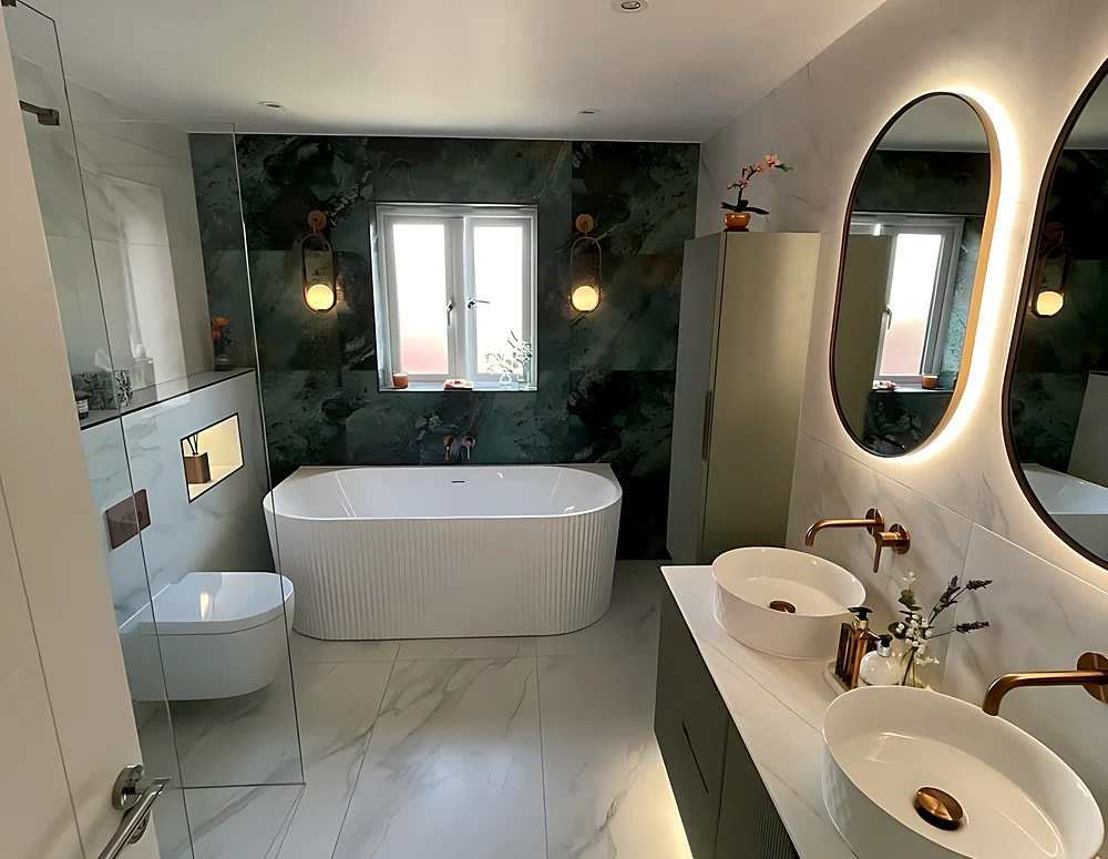 Family bathroom on Canvey Island with a freestanding bath under the window, a green marble-effect wall and a double vanity with two oval LED mirrors