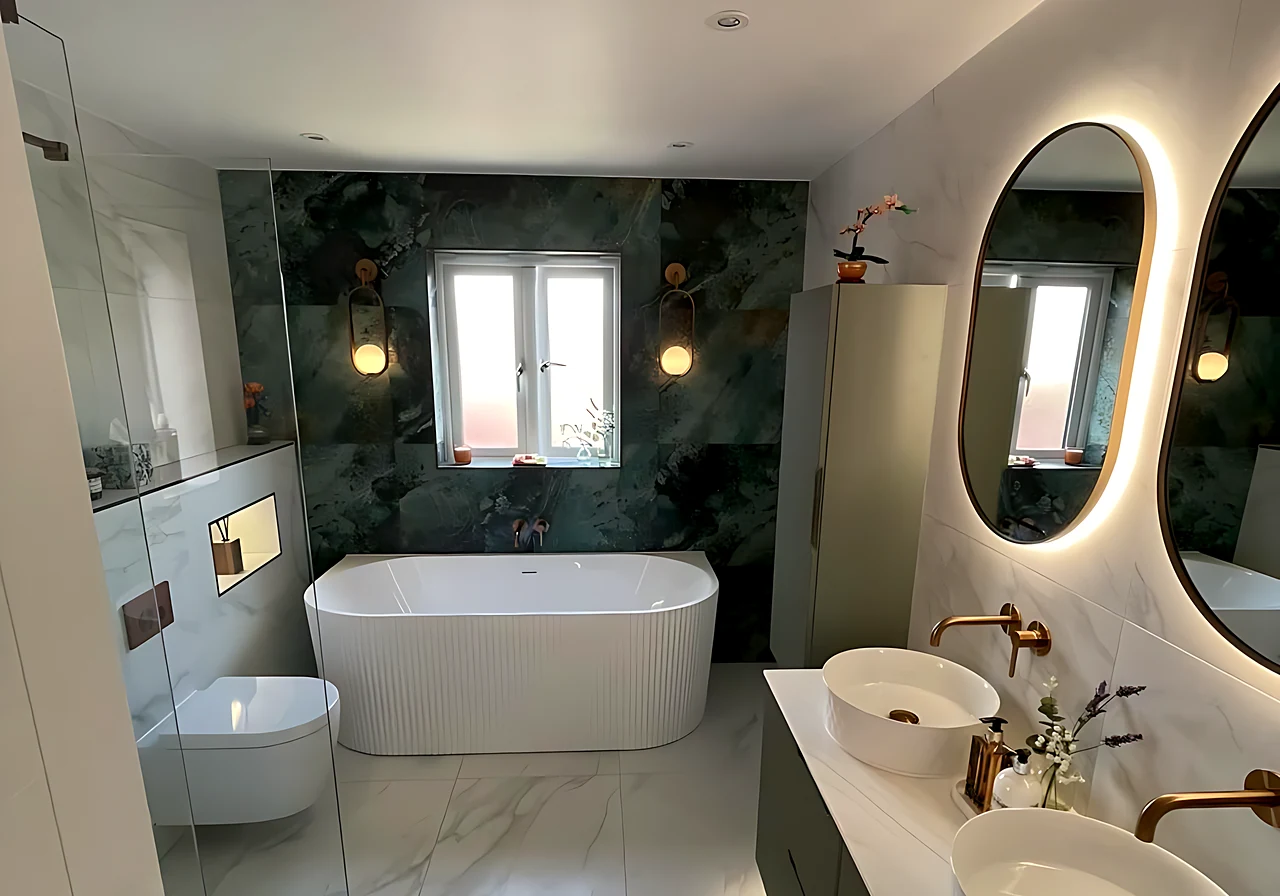 Family bathroom on Canvey Island with a freestanding bath under the window, a green marble-effect wall and a double vanity with two oval LED mirrors