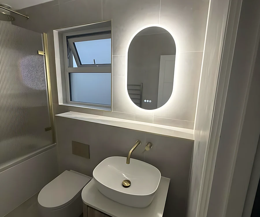 Bathroom with an oval LED mirror, a brushed brass tap and a countertop basin on a wood vanity