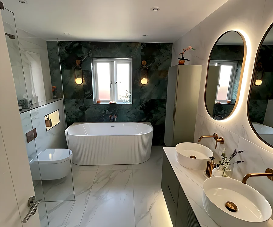 Family bathroom on Canvey Island with a freestanding bath under the window, a green marble-effect wall and a double vanity with two oval LED mirrors