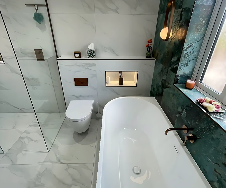 Family bathroom on Canvey Island with a freestanding bath under the window, a green marble-effect wall and a double vanity with two oval LED mirrors