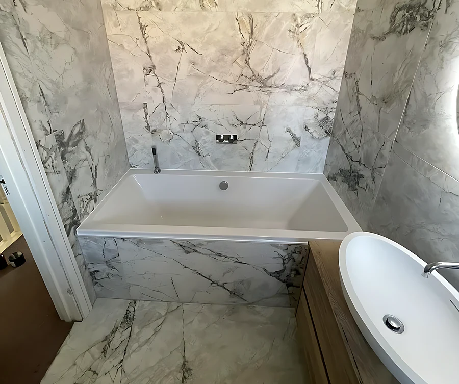 South Woodham Ferrers bathroom with a bath set into marble-effect porcelain on the walls and floor