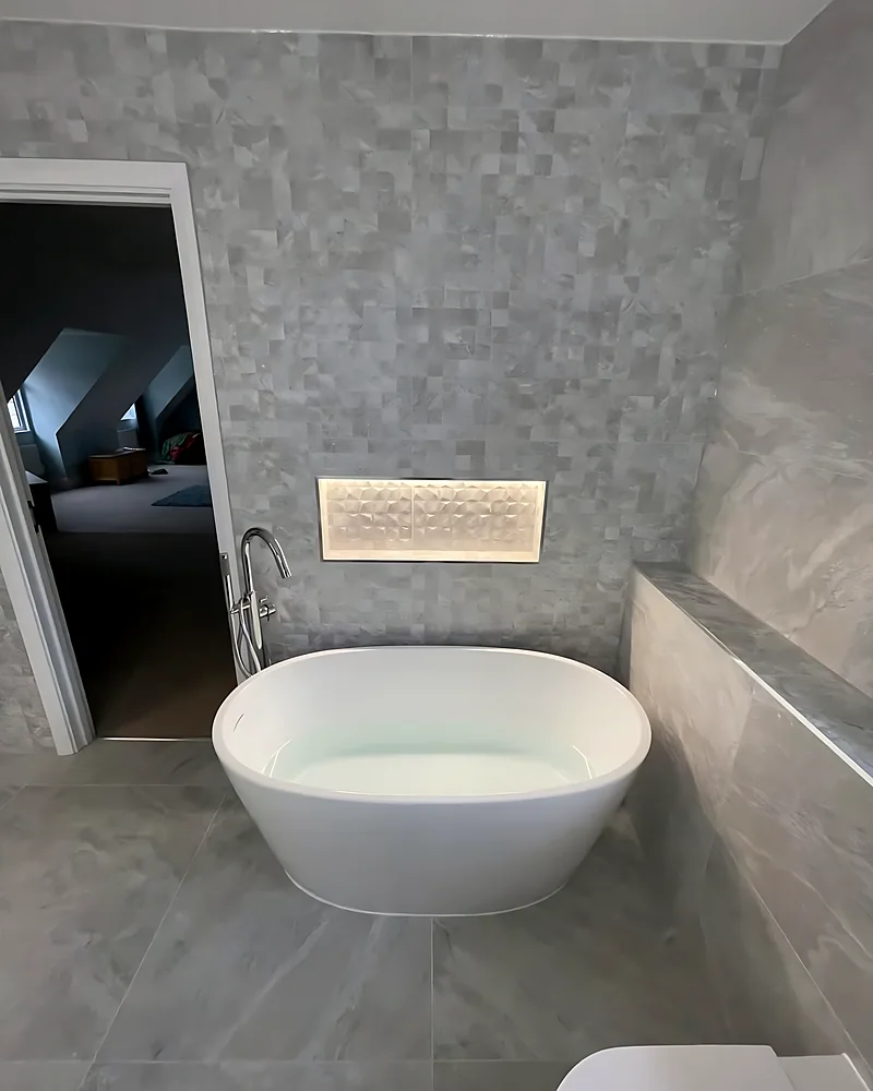Freestanding bath under a lit niche in a Hutton en suite fitted by Gilt Edged Bathrooms